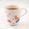 A Colour Changing Mug filled with tea displays vibrant cat illustrations and pink paw prints, elegantly resting on a marble surface.